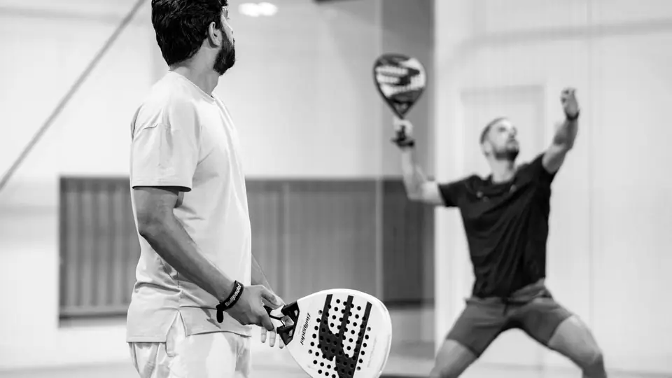 A player watches as his opponent reaches up for an overhead shot.
